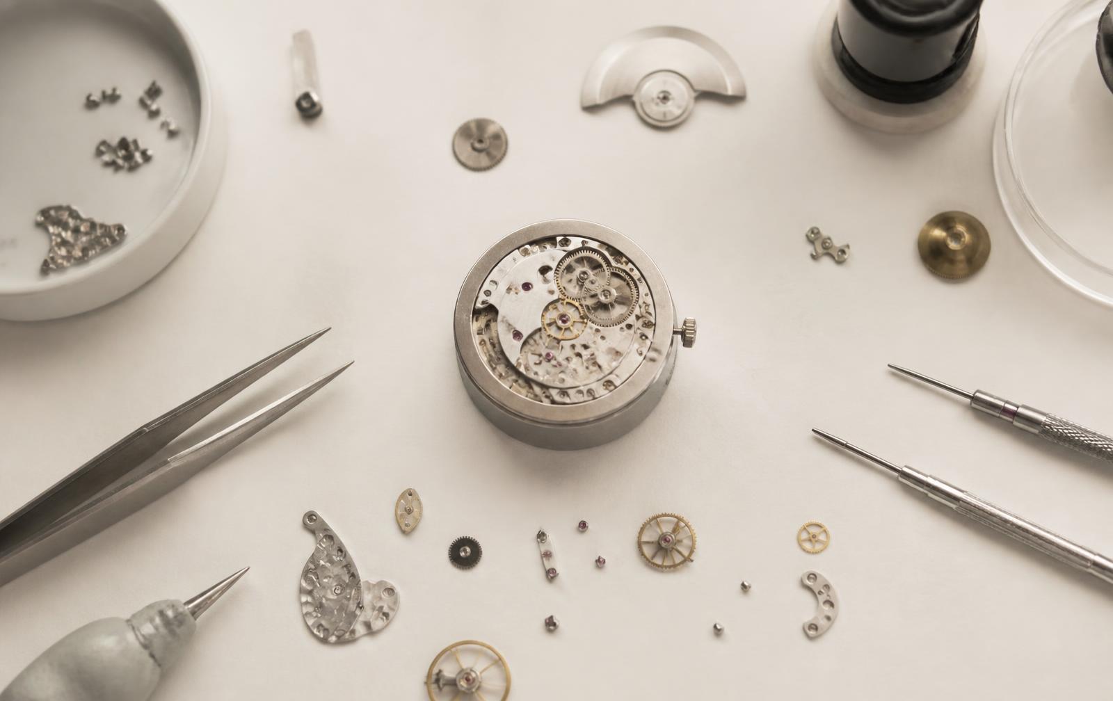 Disassembled mechanical watch movement and watchmaking tools on a bench